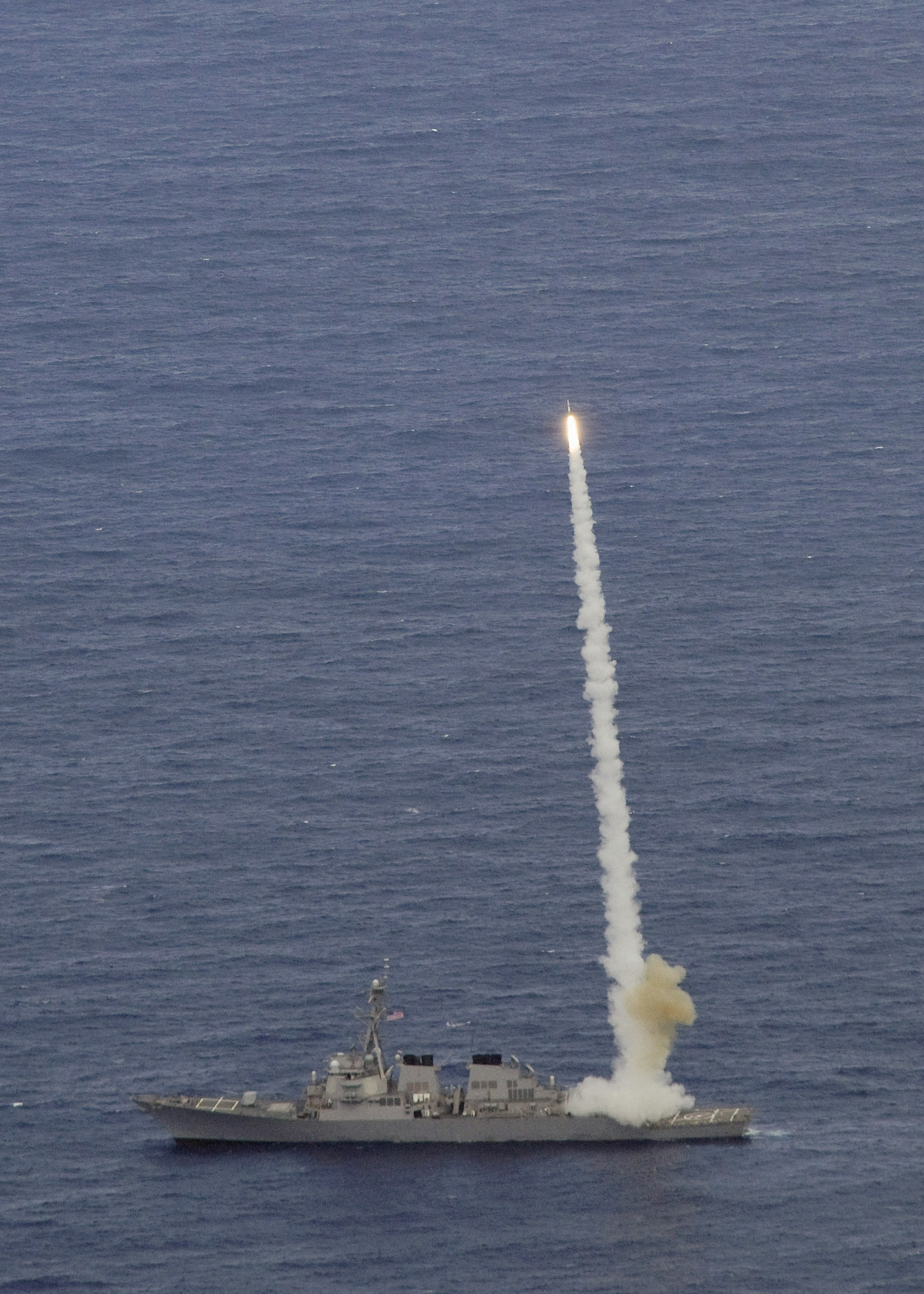 An Arleigh Burke class destroyer launching an SM-2 missile at sea, with the smoke trail of a previous launch beside it.